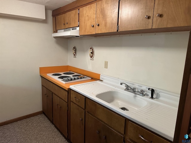 kitchen featuring baseboards, light countertops, under cabinet range hood, a sink, and white electric cooktop