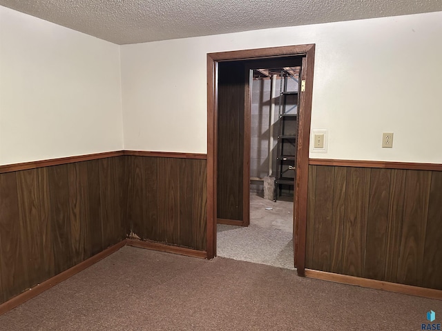 carpeted spare room with a textured ceiling, wood walls, and a wainscoted wall