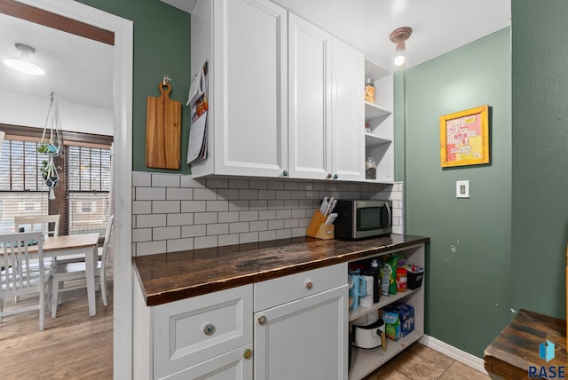 kitchen featuring open shelves, wooden counters, white cabinetry, stainless steel microwave, and backsplash