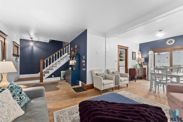 living room featuring stairs, baseboards, wood finished floors, and beamed ceiling