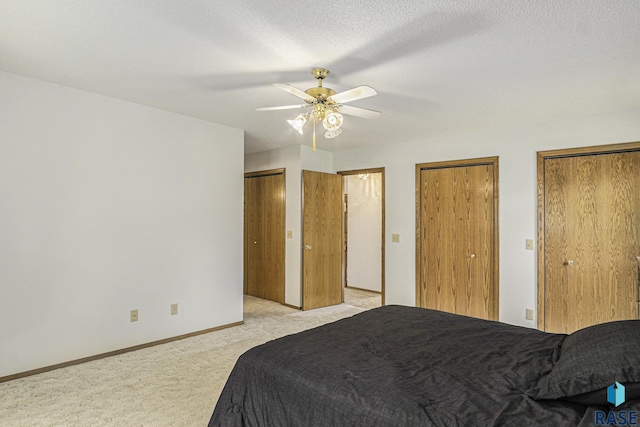 bedroom with a ceiling fan, baseboards, light carpet, and two closets