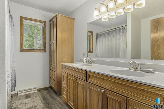 full bath with a sink, double vanity, wood finished floors, and visible vents