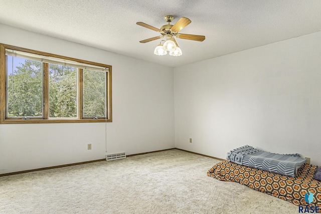 unfurnished bedroom featuring a ceiling fan, a textured ceiling, visible vents, baseboards, and carpet flooring