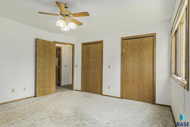 unfurnished bedroom with two closets, baseboards, and carpet floors