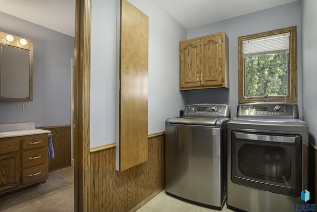 laundry area with cabinet space, wooden walls, washing machine and dryer, and a wainscoted wall