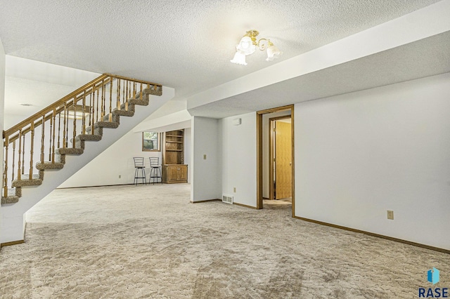 unfurnished living room featuring carpet flooring, a textured ceiling, stairs, baseboards, and visible vents
