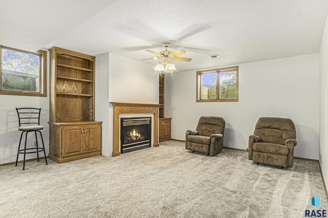 living area featuring a textured ceiling, ceiling fan, a lit fireplace, and carpet