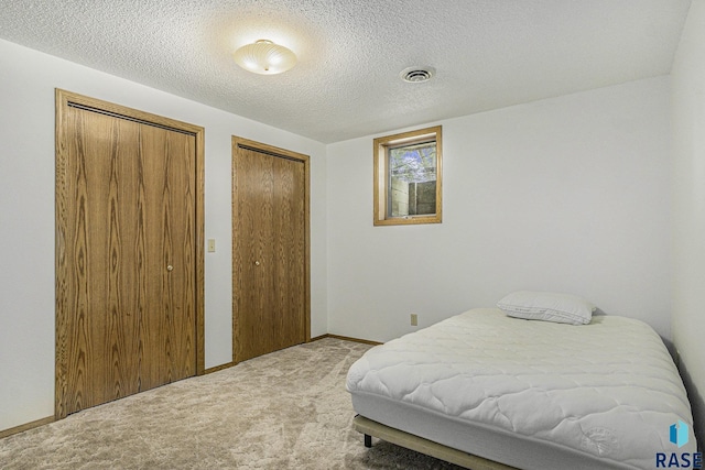 bedroom with two closets, a textured ceiling, and carpet