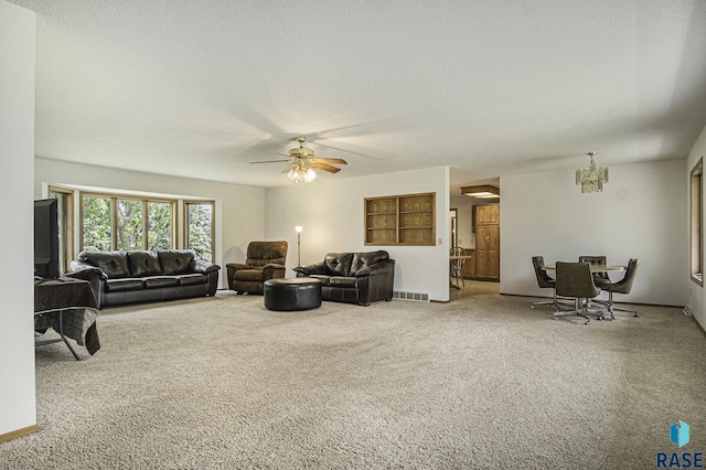 carpeted living room with visible vents, a textured ceiling, and ceiling fan with notable chandelier