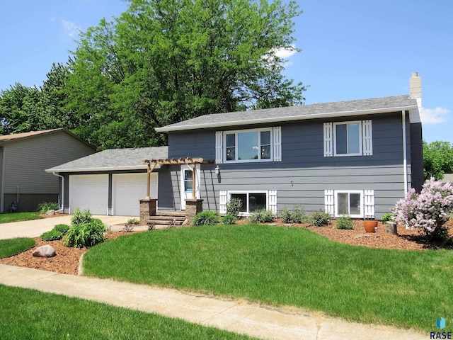 tri-level home featuring an attached garage, a chimney, driveway, and a front yard