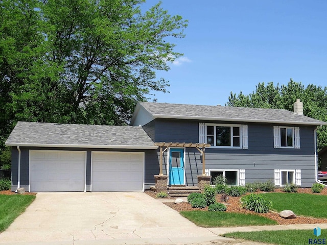 tri-level home with a garage, a chimney, and concrete driveway