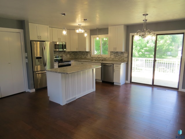 kitchen featuring a kitchen island, backsplash, appliances with stainless steel finishes, white cabinets, and an inviting chandelier