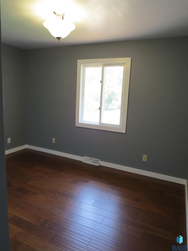 spare room with baseboards, visible vents, and dark wood finished floors