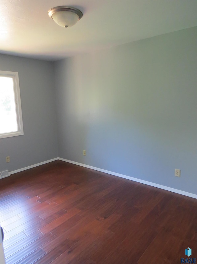 unfurnished room featuring baseboards, dark wood-style flooring, and visible vents