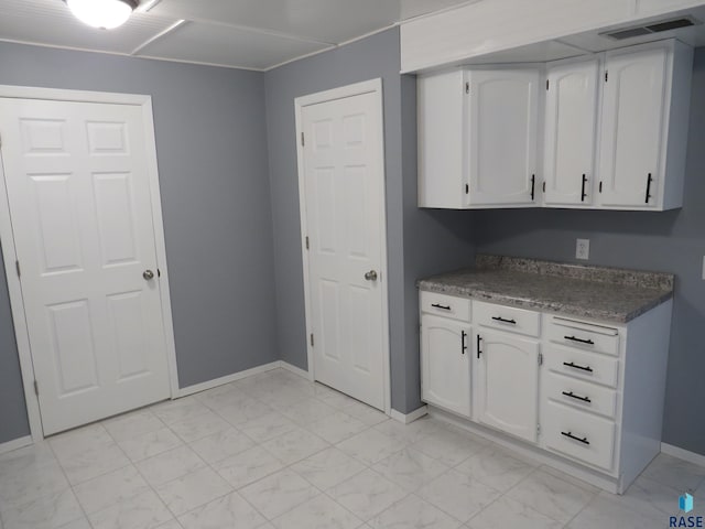 kitchen featuring baseboards, marble finish floor, and white cabinets