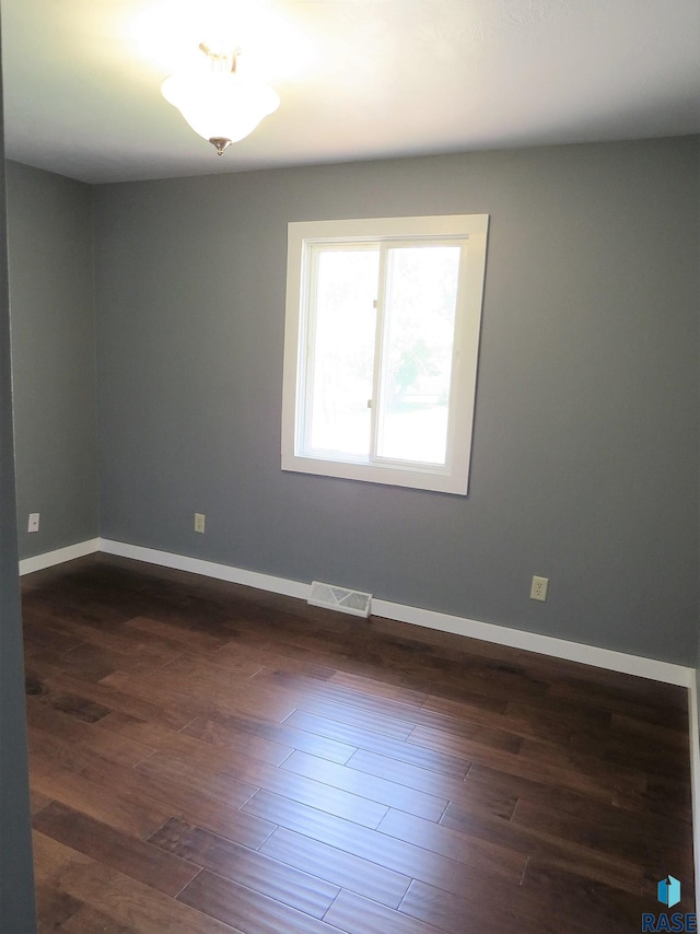 unfurnished room featuring baseboards, dark wood-style floors, and visible vents