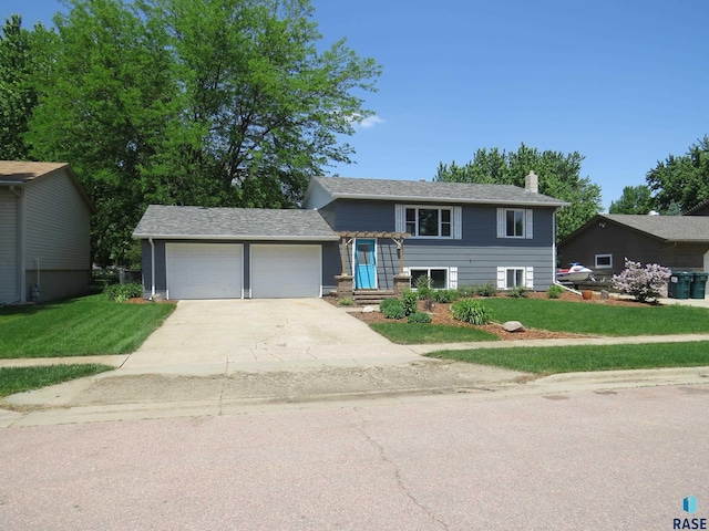 tri-level home featuring a garage, a chimney, driveway, and a front yard