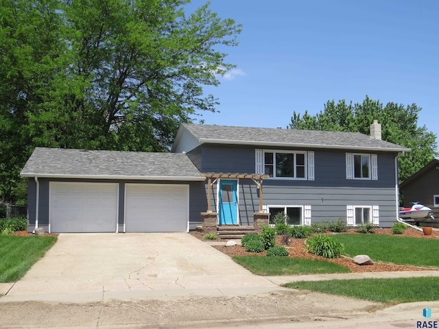 tri-level home with driveway, a chimney, a front yard, and a garage
