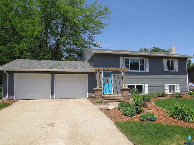 tri-level home featuring a chimney, an attached garage, and driveway