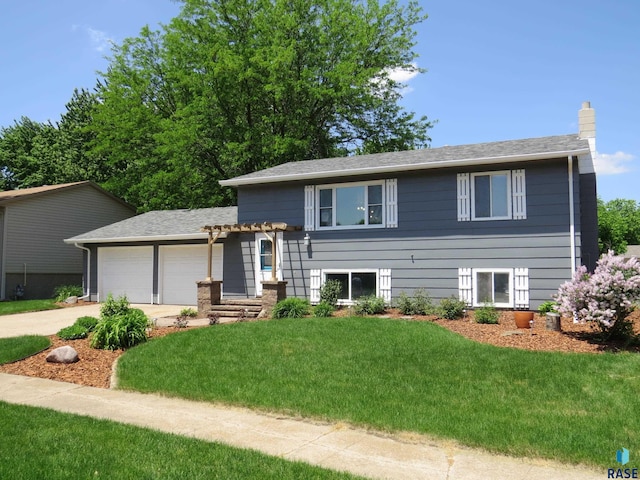 tri-level home featuring concrete driveway, a chimney, a front yard, and a garage