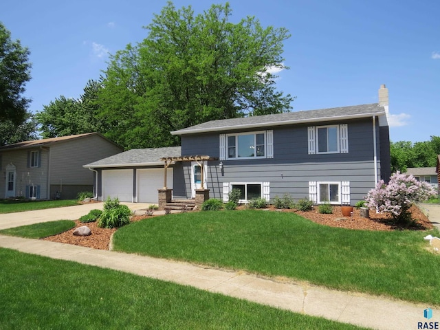 split level home with a chimney, a front yard, central AC, concrete driveway, and an attached garage