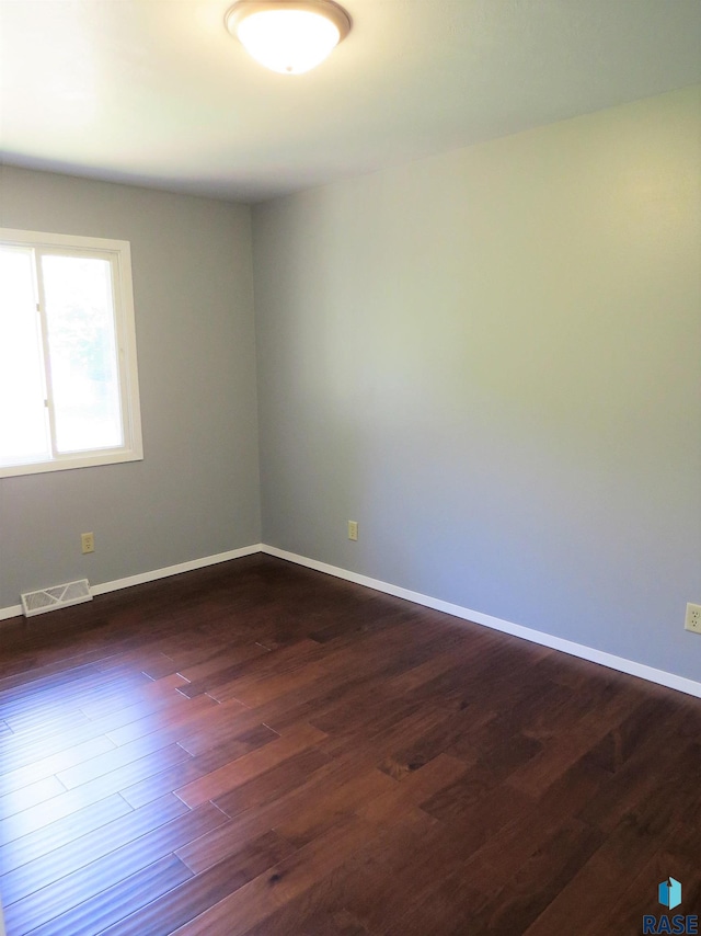 unfurnished room featuring dark wood-style flooring, baseboards, and visible vents
