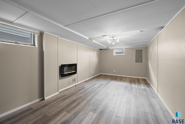 below grade area with a glass covered fireplace, baseboards, electric panel, and wood finished floors
