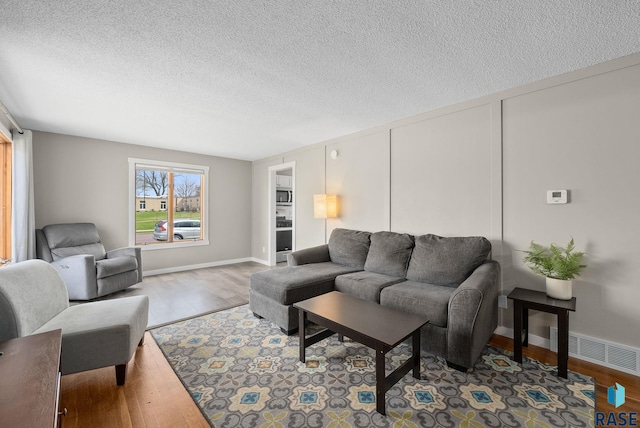 living area with a textured ceiling, visible vents, and wood finished floors