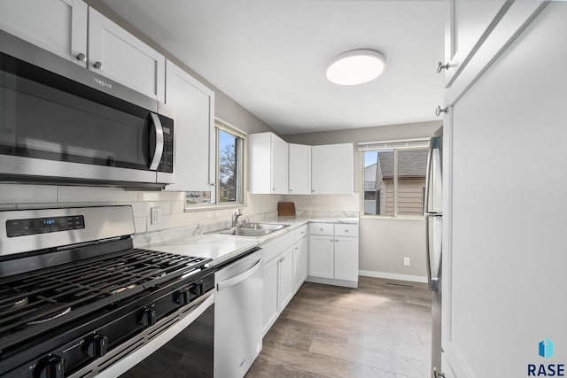 kitchen featuring a sink, light countertops, white cabinets, stainless steel appliances, and light wood-style flooring