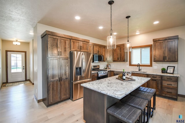 kitchen with backsplash, appliances with stainless steel finishes, a sink, and light wood-style flooring