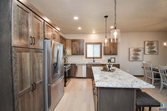 kitchen with a kitchen breakfast bar, a center island, light wood-type flooring, a sink, and appliances with stainless steel finishes