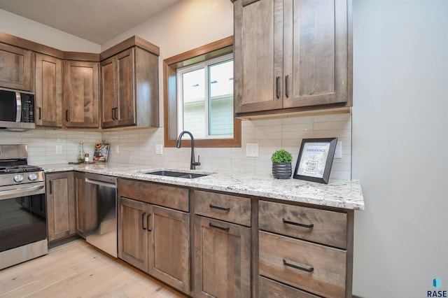 kitchen with a sink, appliances with stainless steel finishes, decorative backsplash, and light stone counters