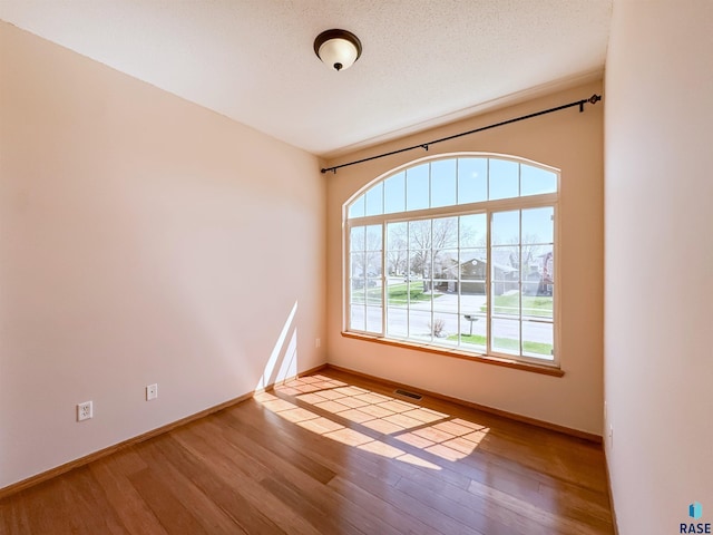 empty room with baseboards, visible vents, and wood finished floors