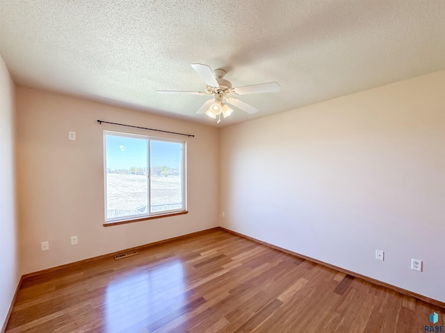 unfurnished room featuring a textured ceiling, a ceiling fan, wood finished floors, and visible vents
