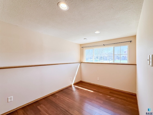 empty room featuring a textured ceiling, baseboards, recessed lighting, and wood finished floors