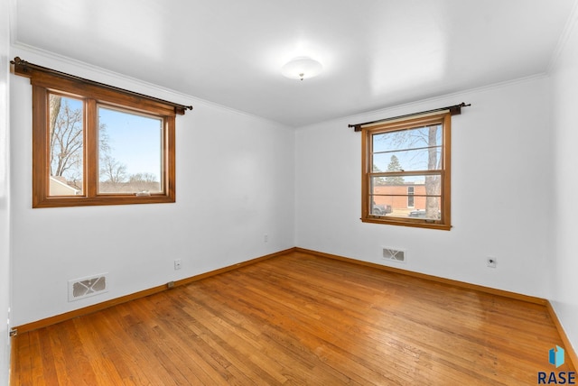 empty room with baseboards, ornamental molding, light wood finished floors, and visible vents