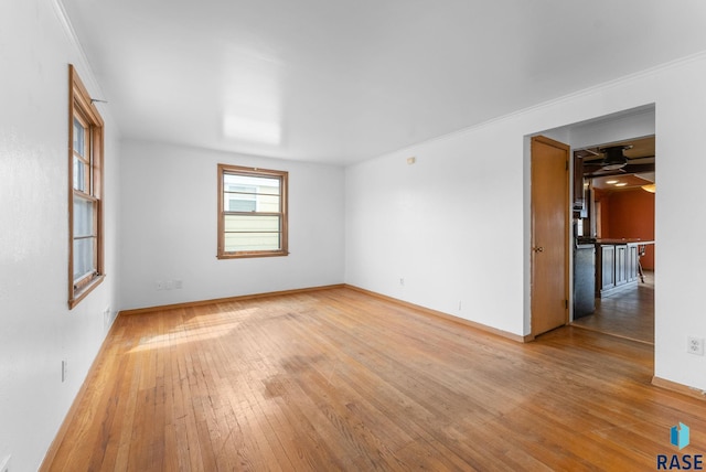 empty room featuring crown molding, baseboards, ceiling fan, and light wood-style flooring