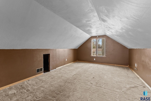additional living space with a textured ceiling, carpet, baseboards, lofted ceiling, and visible vents