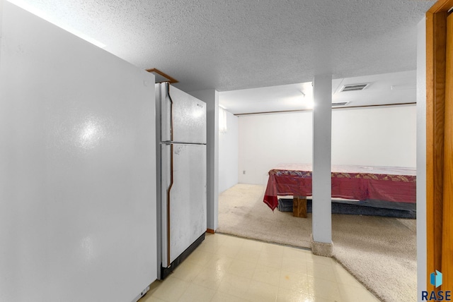 finished basement featuring freestanding refrigerator, a textured ceiling, light colored carpet, and light floors