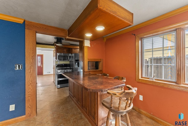 kitchen featuring a ceiling fan, dark countertops, appliances with stainless steel finishes, a breakfast bar, and light tile patterned flooring