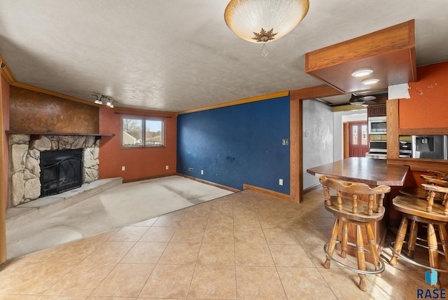 carpeted living room featuring tile patterned floors, a stone fireplace, and baseboards
