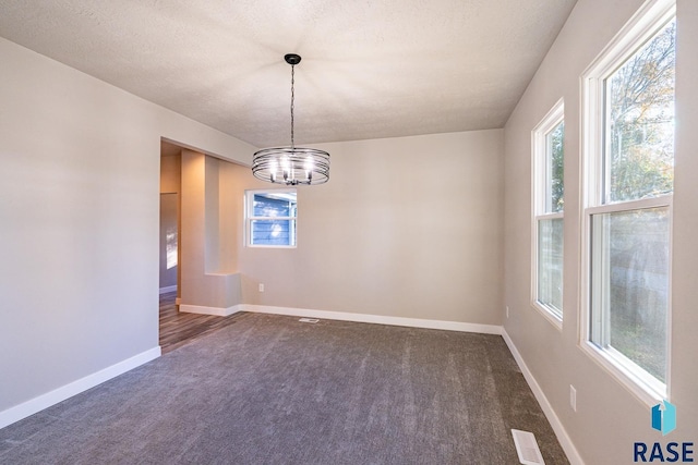 empty room featuring a notable chandelier, carpet floors, a textured ceiling, baseboards, and visible vents