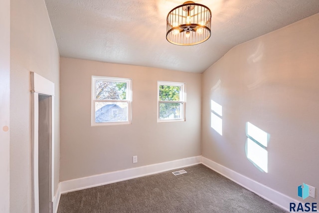 empty room with a textured ceiling, dark carpet, baseboards, vaulted ceiling, and visible vents