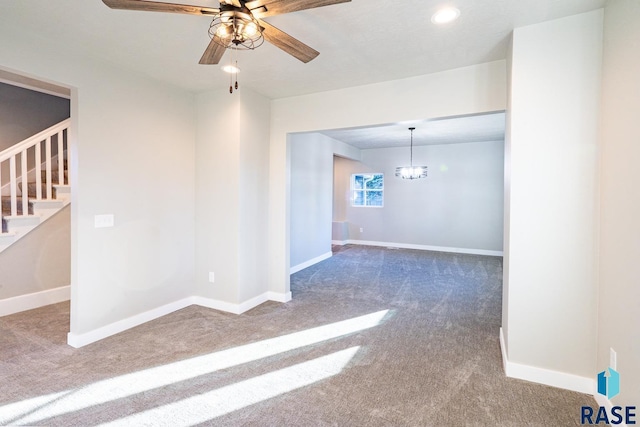 carpeted empty room featuring stairway, baseboards, and ceiling fan with notable chandelier