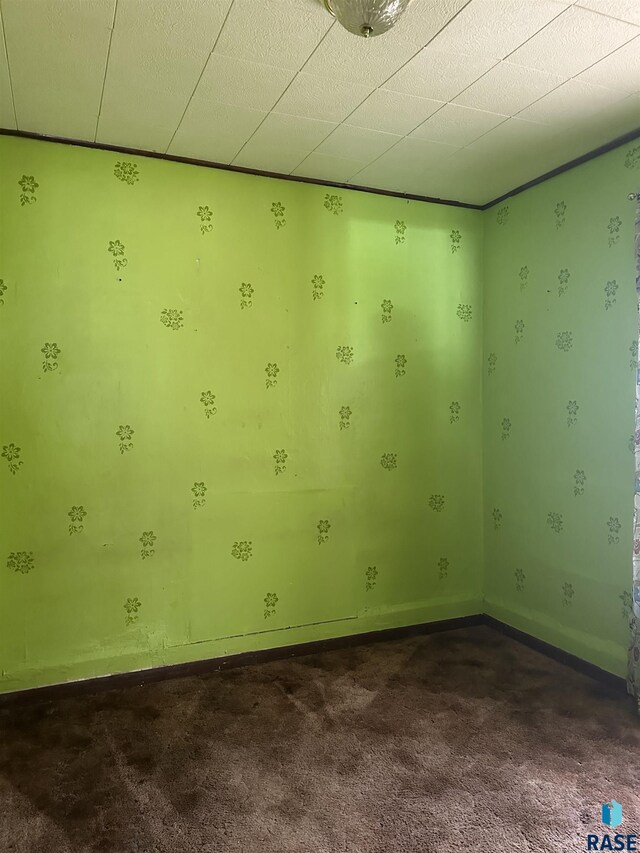 spare room with baseboards and dark colored carpet