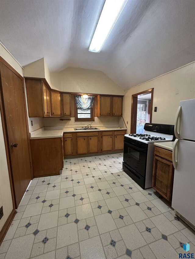 kitchen featuring freestanding refrigerator, lofted ceiling, brown cabinets, range with gas cooktop, and a sink
