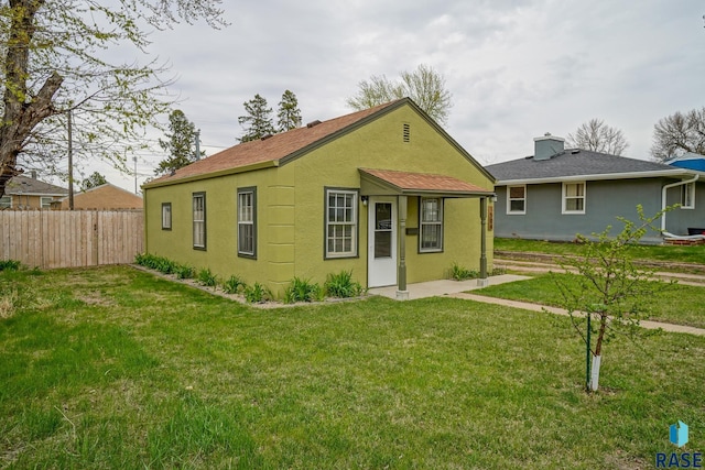 back of house with a lawn, stucco siding, a chimney, and fence