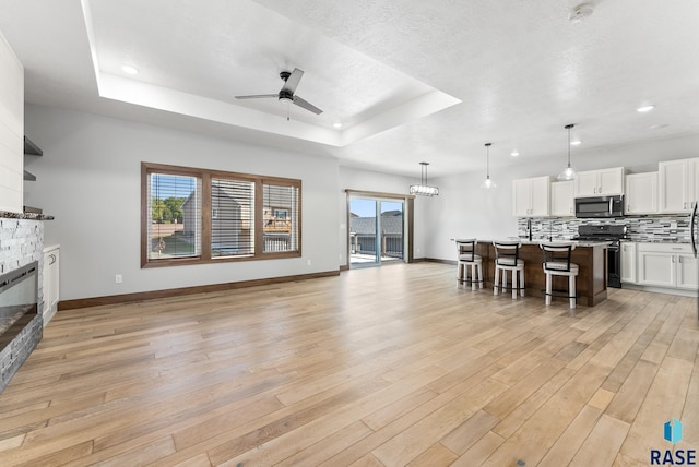living room with ceiling fan, a raised ceiling, light wood-style floors, a fireplace, and baseboards