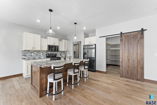 kitchen featuring a barn door, black range with gas cooktop, baseboards, white cabinetry, and stainless steel refrigerator with ice dispenser