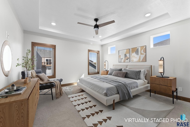 bedroom with light colored carpet, recessed lighting, a raised ceiling, and baseboards